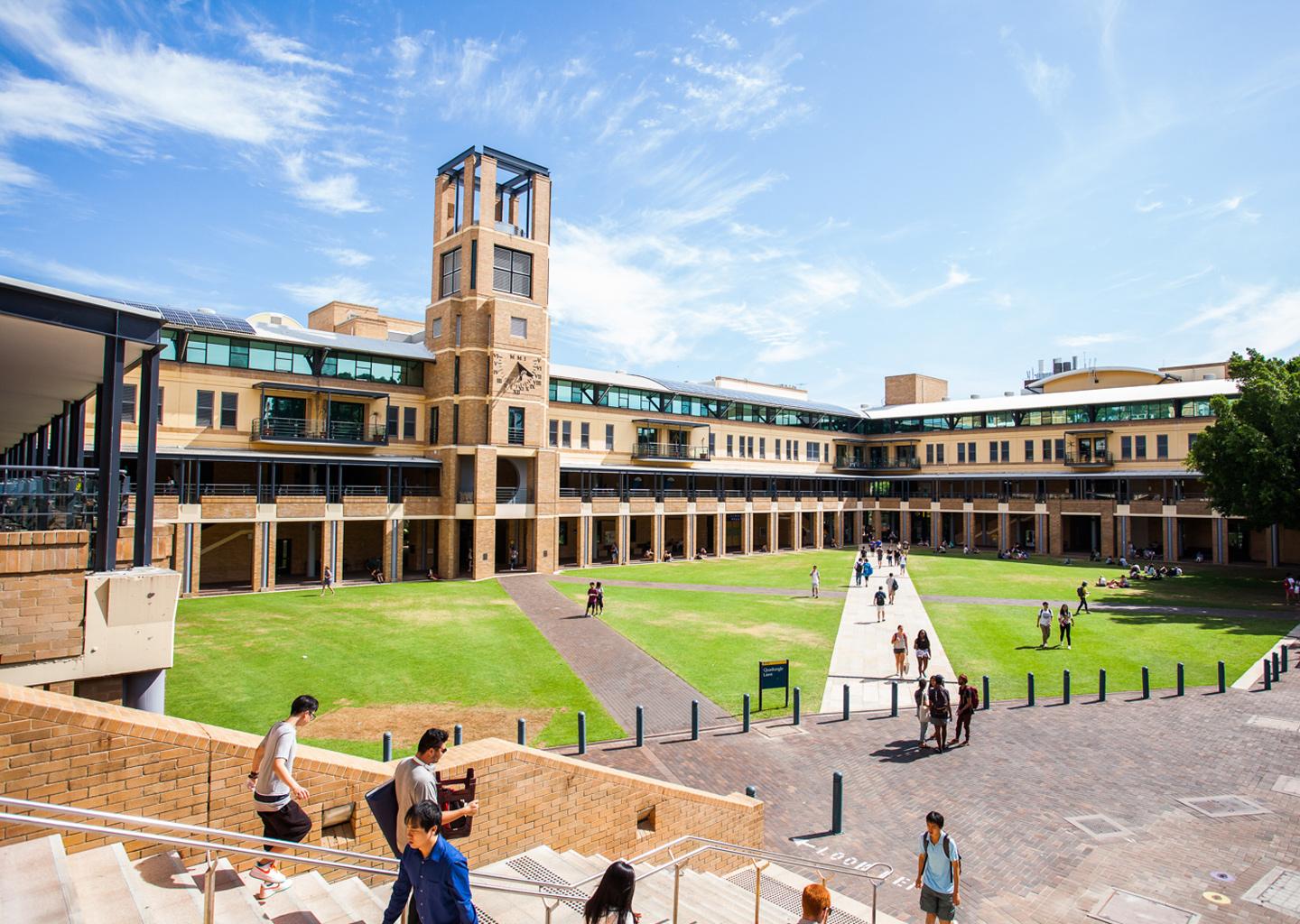 Students walking across the central lawn of the UNSW Sydney Quadrangle, surrounded by brick buildings.