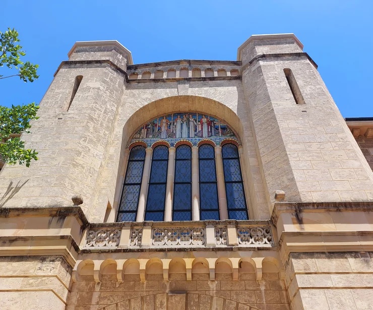 Close-up of a heritage sandstone university entrance with tall arched windows, decorative artwork and two square towers.
