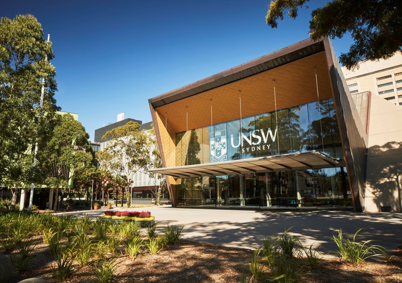Glass-fronted Clancy Auditorium at UNSW Sydney, surrounded by trees and landscaped gardens.
