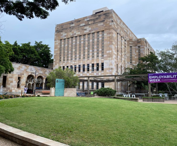 View across the lawn at Campbell Place, featuring a large sandstone university building, outdoor seating, and an Employability Week banner.