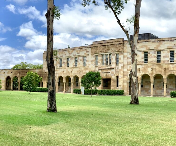 Sandstone academic building with arched colonnades overlooking the green lawn of the University of Queensland’s Great Court.